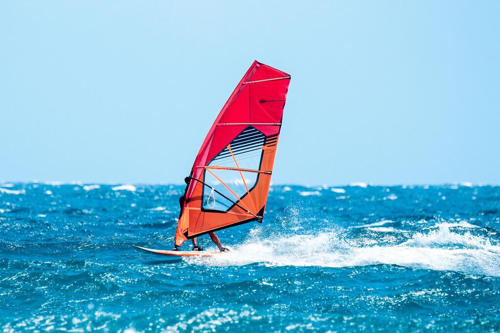 pessoa em uma prancha com vela praticando windsurf