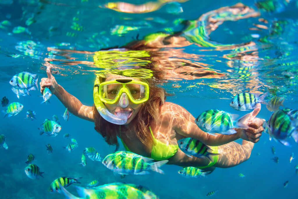 mulher embaixo da água usando óculos de proteção e praticando mergulho com snorkel