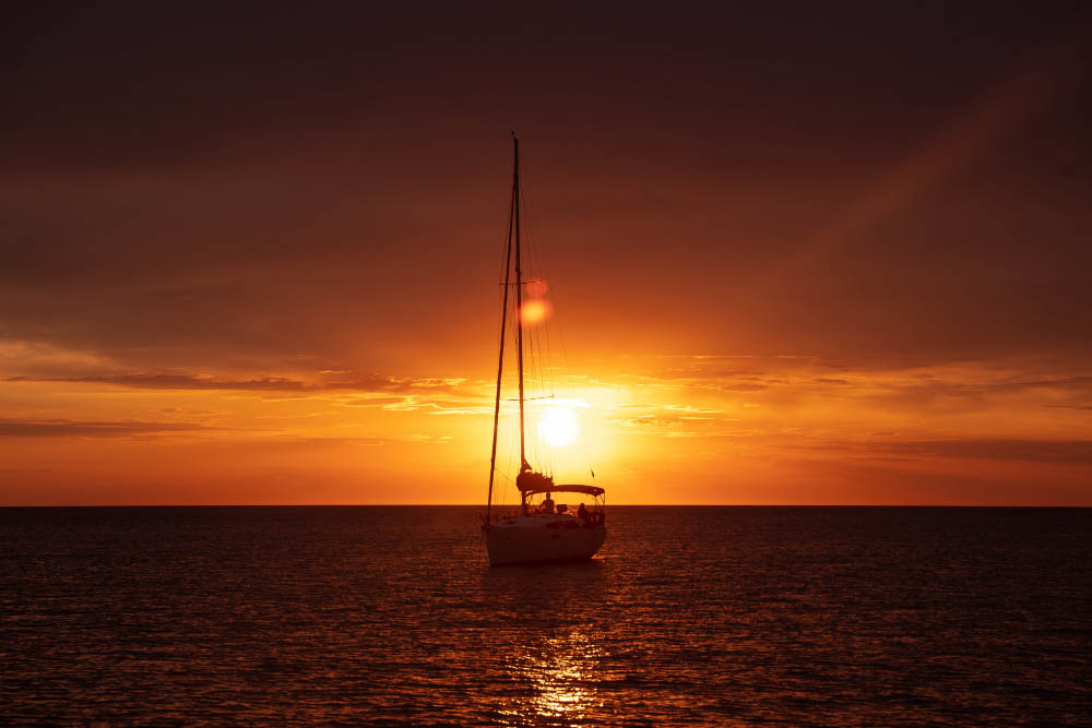 embarcação no mar ao pôr do sol, representando o comparativo entre barco a vela vs lancha