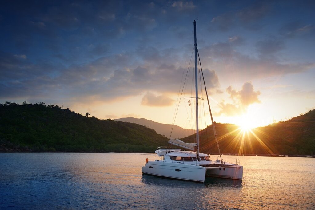 Um catamarã à vela no oceano ao pôr do sol, com tons quentes iluminando a cena serena.