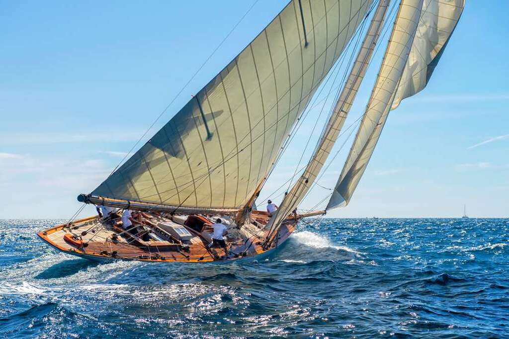 Regata de veleiro com equipes de marinheiros navegando em alto mar sob céu claro e vento forte.